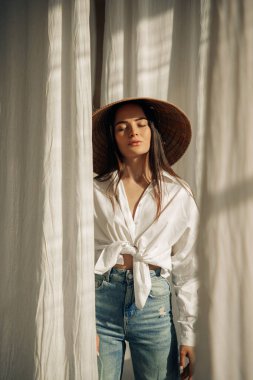 Genç bir kadın rahat ve gözleri kapalı duruyor kot pantolon, beyaz gömlek ve Vietnam şapkası içinde..
