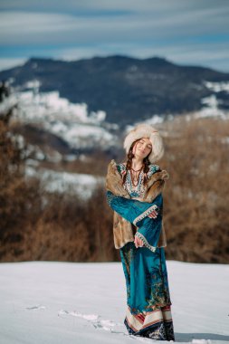 Kürk şapka, yelek ve elbise giymiş genç bir kadın, karla kaplı Karpatlar 'ın güzel manzarasına karşı karın üzerinde duruyor..