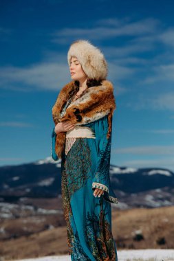 Kürk şapkalı, yakalı, yakalı bir tilki gibi duran genç bir kadın karla kaplı Karpatlar 'ın dağları ve gökyüzünün güzel manzarasına karşı..