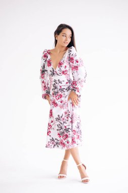 Genç bir kadın beyaz arka planda şık bir çiçek desenli elbise giyiyor. Tam boy vücut görüntüsü. İzole edilmiş resim.