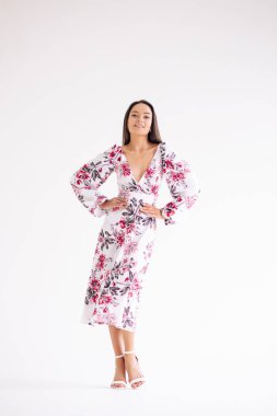 Genç bir kadın beyaz arka planda şık bir çiçek desenli elbise giyiyor. Tam boy vücut görüntüsü. İzole edilmiş resim.