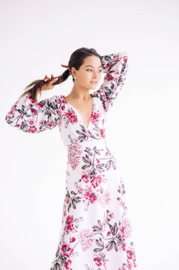 Genç bir kadın beyaz arka planda şık bir çiçek desenli elbise giyiyor. İzole edilmiş resim.