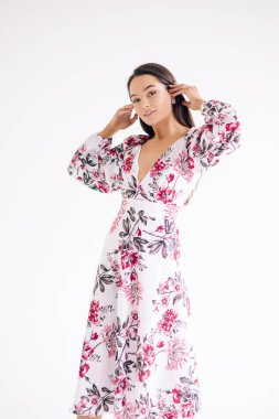 Genç bir kadın beyaz arka planda şık bir çiçek desenli elbise giyiyor. İzole edilmiş resim.