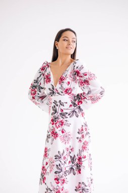 Genç bir kadın beyaz arka planda şık bir çiçek desenli elbise giyiyor. İzole edilmiş resim.