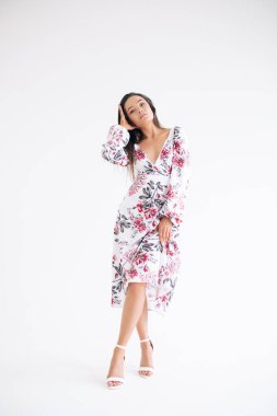 Genç bir kadın beyaz arka planda şık bir çiçek desenli elbise giyiyor. Tam boy vücut görüntüsü. İzole edilmiş resim.