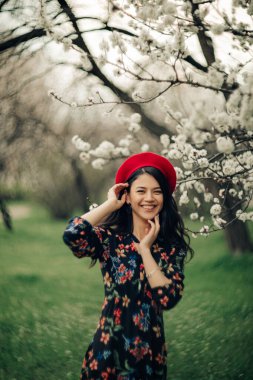 Young brunette woman has a fun in garden among the spring blossoming apricot trees.