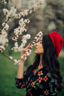 Portrait of young brunette woman in beret enjoying among the spring blossoming apricot trees.
