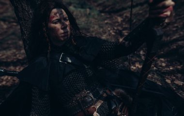Ortaçağ savaşçısı kılığındaki zincirli kadın ormanın ortasında, ağacın yanında oturur ve dinlenir. Yakın çekim..