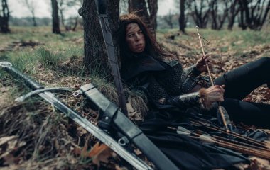 Ortaçağ savaşçısı görüntüsünde zincirli kadın ormanın içinde, ağacın yanında yatıyor ve dinleniyor..