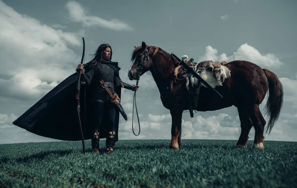 中世纪战士形象中的女人戴着锁链 手里拿着弓 站在田边的马旁边 — 图库照片