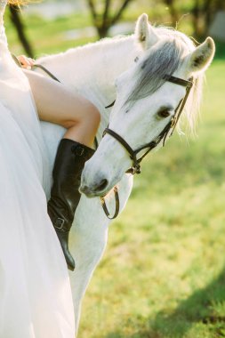 Deri çizmeli çıplak kadın, beyaz atın üstünde oturuyor..