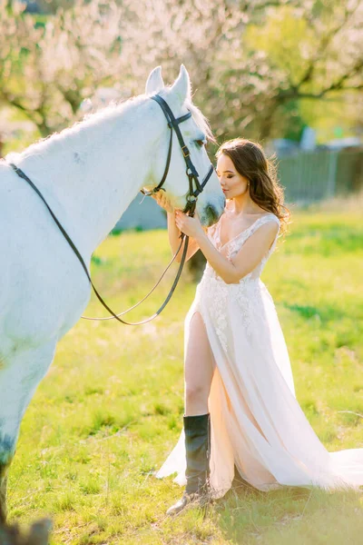 Noiva Vestido Branco Longo Fica Perto Cavalo Branco Abraça Jardim — Fotografia de Stock