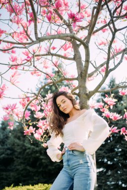 Genç bir kadın bahar bahçesinde, çiçek açan manolya ağacının altında duruyor..