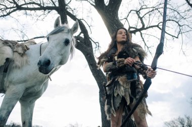 Antik savaşçı Amazon suretinde bir kadın bir yay atar ve ormanın ortasında atının yanına nişan alır..