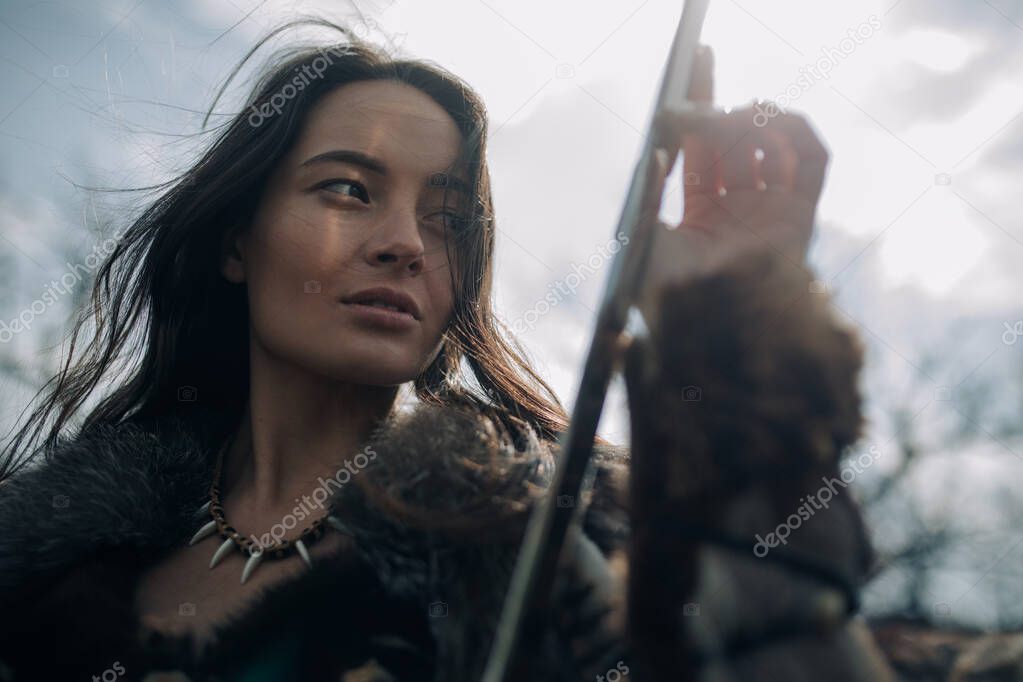 Portrait of woman in image of ancient warrior amazon with sword in her hands on background of sky.