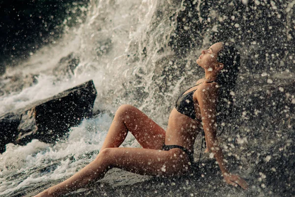 美丽而性感的女人 穿着比基尼 坐在瀑布流淌的溪流下 闭目养神地欣赏落水 — 图库照片