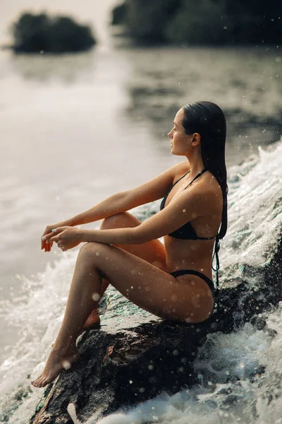 美しいセクシーな女性は滝の流れの下でビキニに座って 川を見て — ストック写真