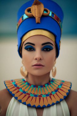 Portrait of young woman in image of ancient egyptian queen Nefertiti against background of sandy desert and blue sky.