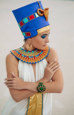 Portrait of young woman in image of ancient egyptian queen Nefertiti against background of sandy desert.