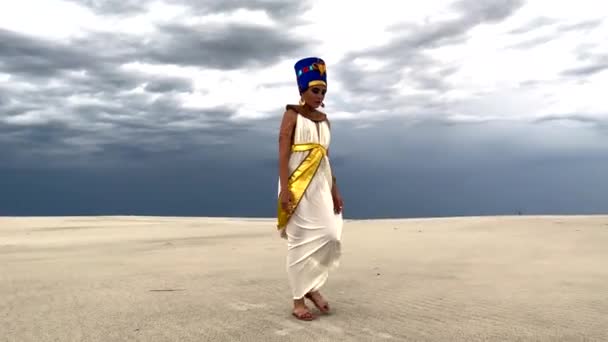 在雷雨的背景下 古埃及女王奈夫提提的画像中的年轻女子在沙质的沙漠中行走 — 图库视频影像