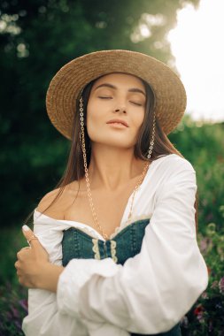 Hasır şapkalı genç bir kadının portresi Çiçekler arasındaki çayırda gözleri kapalı.