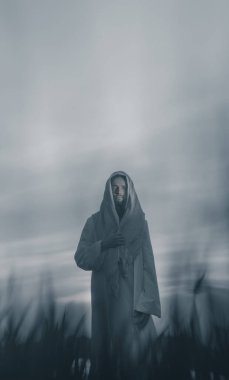 İsa, geleneksel beyaz cübbesiyle çayırlarda yürüyor gün batımında gökyüzüne karşı..