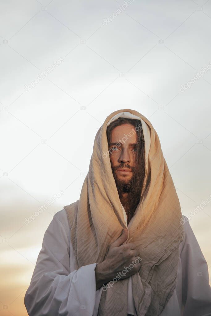 Jesus Christ stands in his traditional white robe against sky background. Portrait.