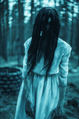 Uzun siyah saçlı korkunç hayalet zombi suretinde bir kız karanlık ormanın içinde taş kuyusunun arkasında duruyor..