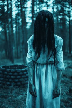 Uzun siyah saçlı korkunç hayalet zombi suretinde bir kız karanlık ormanın içinde taş kuyusunun arkasında duruyor..