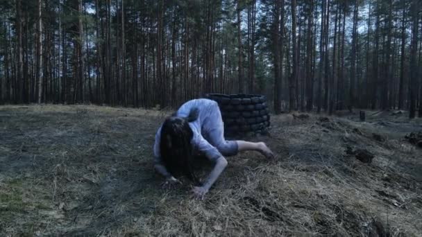怖いゴーストゾンビのイメージで長い黒い髪の女の子は石の近くの森の中で地面にクロールします ハロウィンのコンセプト — ストック動画