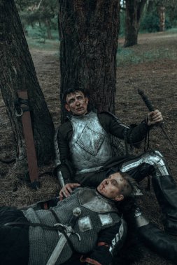 İki yorgun ortaçağ savaşçısı zırhlı şövalyeler ağaçların altında kılıçlarıyla dinleniyorlar..