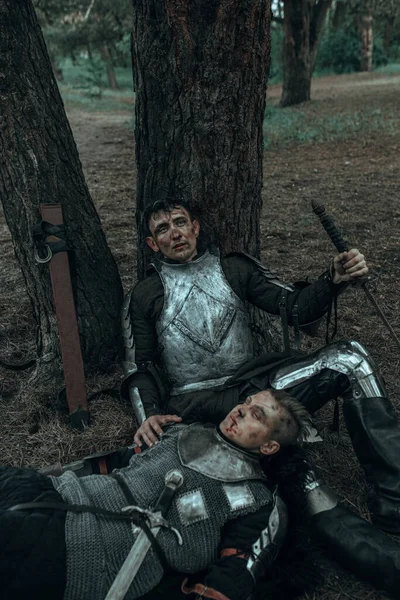 两个穿着锁链甲的疲惫的中世纪武士拿着剑躺在树下的森林里 — 图库照片
