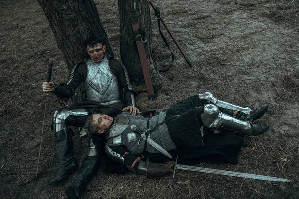 两个穿着锁链甲的疲惫的中世纪武士拿着剑躺在树下的森林里 — 图库照片
