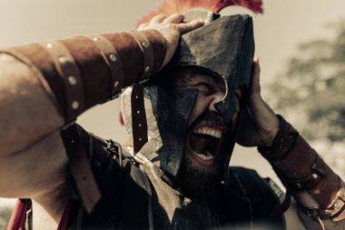 Öfkeyle çığlık atan eski Spartalı savaşçı gökyüzü arka planına karşı savaş elbisesi giymiş..