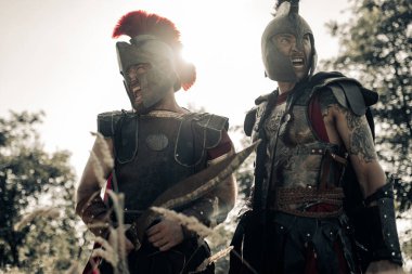 Öfkeyle bağıran iki kişinin portresi. Zırhlı ve miğferli eski Spartalı savaşçılar..