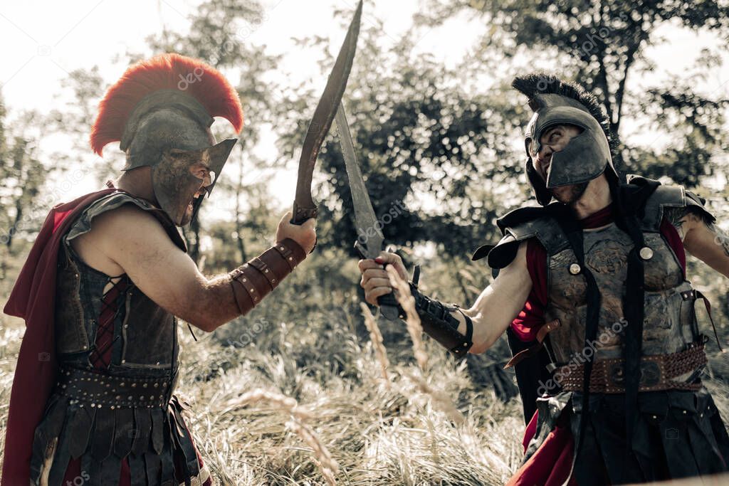 Battle with swords between two ancient greek or roman warriors in battle dress and cloaks on meadow.