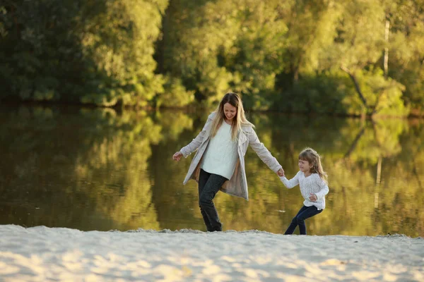 Anne, nehir kıyısındaki sahilde yürürken çığlıklar atan kaprisli kızını kendi eliyle yönlendiriyor..