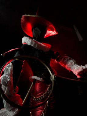 Kırmızı ve siyah soytarı ya da konik şapkalı palyaço kostümü ve kırmızı dramatik ışıkla karanlıktan çıkan yakalı gizemli kişi. Cadılar Bayramı partisi için kostüm, kostüm. Yakın plan..