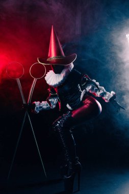 Kırmızı ve siyah kostümlü soytarı ya da palyaço kostümlü, elinde köpük değnekleri olan kırmızı ve mavi dumanla çarpıcı bir şekilde aydınlatılmış gizemli soytarının dinamik görüntüsü. Cadılar Bayramı karakter teması