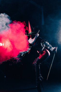 Kırmızı ve siyah kostümlü soytarı ya da palyaço kostümlü, elinde köpük değnekleri olan kırmızı ve mavi dumanla çarpıcı bir şekilde aydınlatılmış gizemli soytarının dinamik görüntüsü. Cadılar Bayramı karakter teması