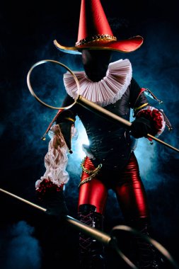 Uzun şapkalı, beyaz yakalı ve altın zincirli siyah arka planlı, özenle hazırlanmış kırmızı ve siyah kostümlü dramatik bir soytarı karakteri. Cadılar Bayramı karakter teması.