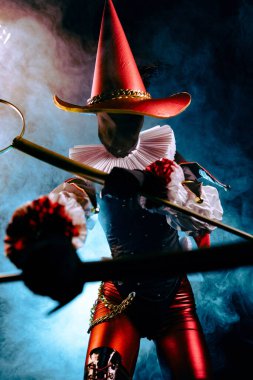 Karanlık soytarı ya da palyaço figürünün dramatik yakın plan Cadılar Bayramı karakteri canlı kırmızı ve siyah bir kostüm içinde, tiyatro ışığıyla aydınlatılmış ve dumanla çevrili..