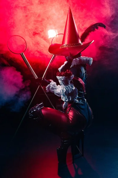 Kırmızı ve siyah kostümlü gizemli soytarı ya da palyaço figürünün dinamik ve dramatik çekimi kalın kırmızı duman ve ışığın arka planına şiddetle karşı duruyor. Cadılar Bayramı karakter teması.