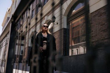 Kendine güveni düşük, iri yarı, siyah erotik iç çamaşırlı ve deri ceketli bir kadın. Şehir caddesinde, bina ve dekoratif korkuluklara yakın şık bir model, vücut pozitifliğini destekliyor..