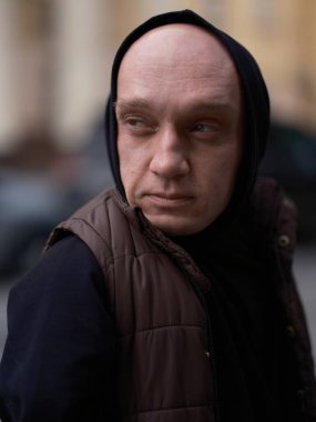 Şehir caddesinde cüceleri olan ciddi bir adamın yakın plan portresi. Kapüşonlu, yoğun bir şekilde başka yöne bakıyor. Benzersiz özellikleri olan etkileyici bir birey..