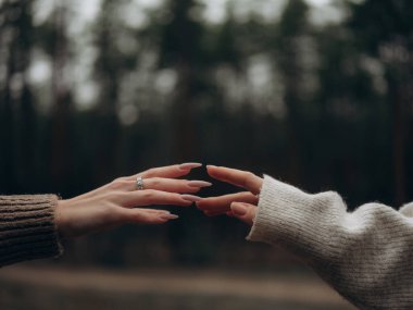 Lezbiyen çift ellerinin birbirine uzandığı yakın plan. Bir el elmas nişan yüzüğü takıyor. Evlilik teklifi, bağlılık, aşk ve LGBT evliliği kavramı.