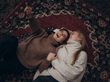 Mutlu genç lezbiyen çift gerçekten gülüyor süslü halıya uzanıp işaret ediyorlar. Eğlence, rahatlama ve çeşitli LGBT ilişkilerinde paylaşılan mutlu an.