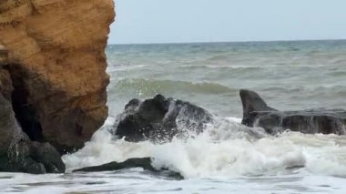 Güçlü deniz dalgalarının Odessa yakınlarındaki Karadeniz kıyısında kayaları kaplayan deniz yosunlarına çarpıp sıçrayan dinamik yakın çekim görüntüsü ve dokulu sarı kil kayalıklar. Ham doğa gücü kavramı.