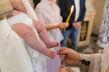 Ortodoks vaftiz töreni sırasında rahibin ellerinin bebeğin bacaklarını meshedişinin yakın çekimi. Çocuğa, ritüele, saflığa ve arka planda yanan mumu olan aileye odaklan.