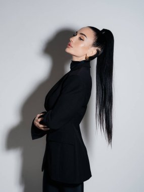 Yandan bakıldığında zarif, genç bir kadın, siyah ceketli balıkçı yaka, yüksek atkuyruklu bir yaka. Profesyonel kendine güvenen kadın model stüdyo portresi. Güzellik stili cazibe konsepti.